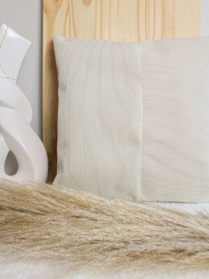 Housse de coussin en velours côtelé écru. Différentes orientations des rayures. Fond en bois et fleur de pampa